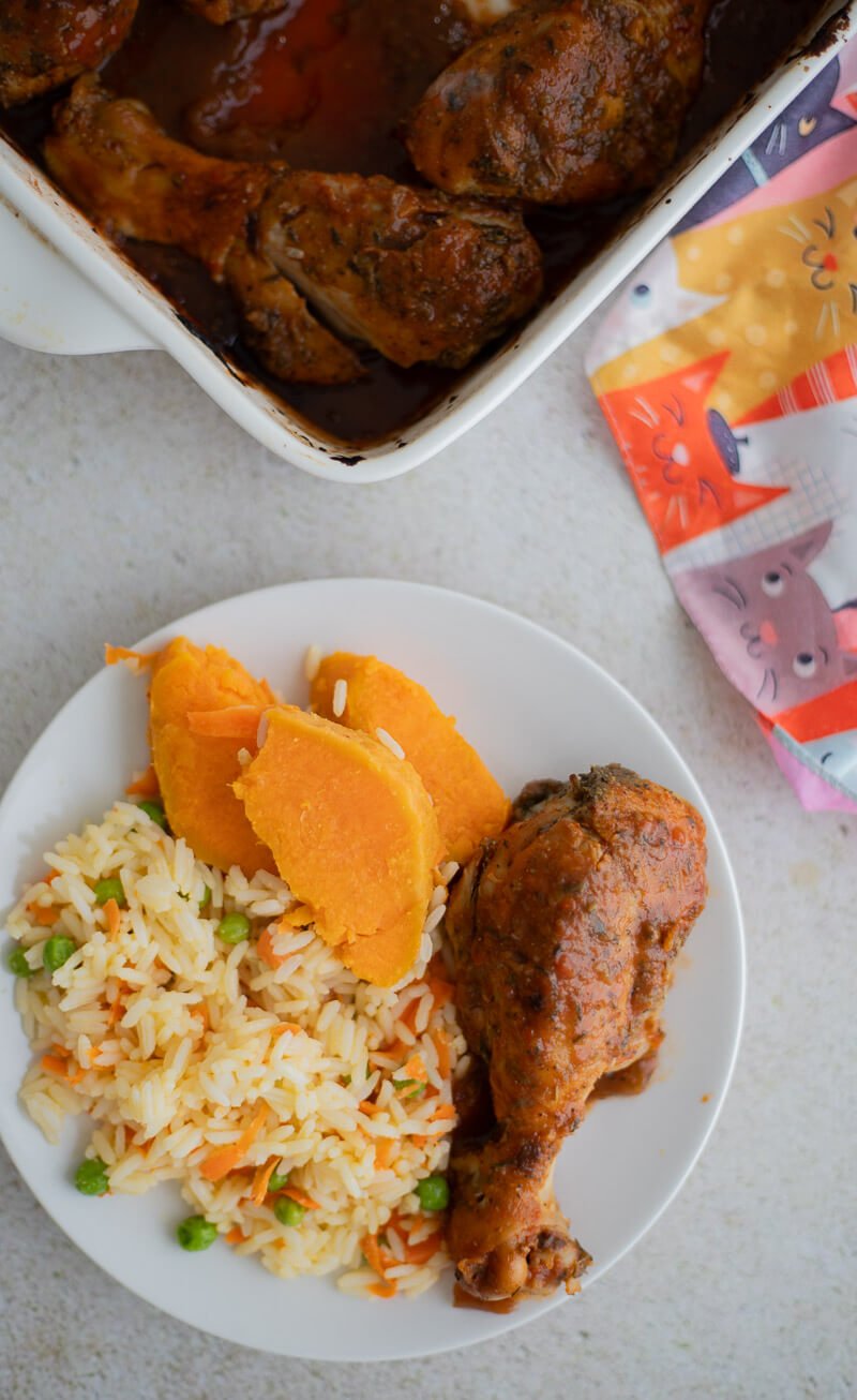 Plate of baked chicken served with vegetable rice and slices of boiled pumpkin.