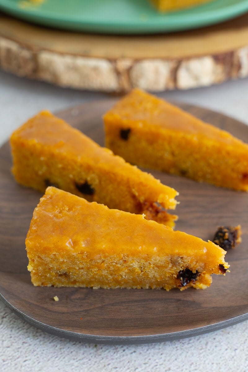 Triangular slices of golden cornmeal pone with raisins on a wooden plate, showing the soft sticky top and moist interior