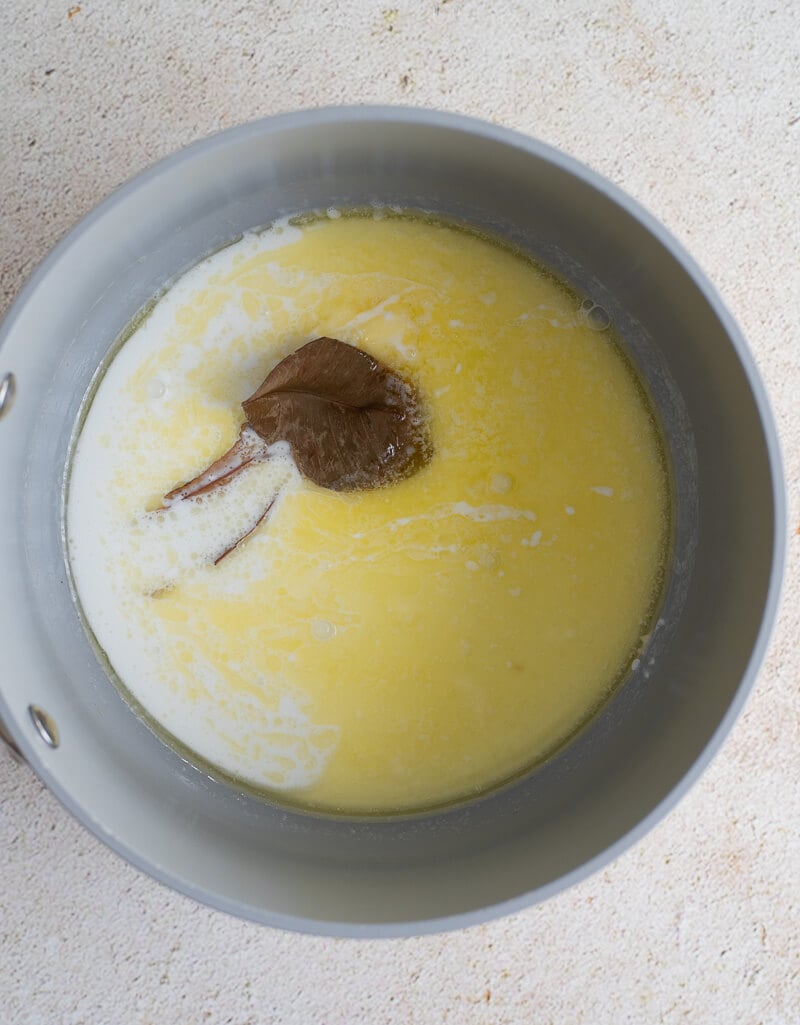 Saucepan with melted butter, coconut milk, and bay leaves simmering for the Trinidad cornmeal pone batter.