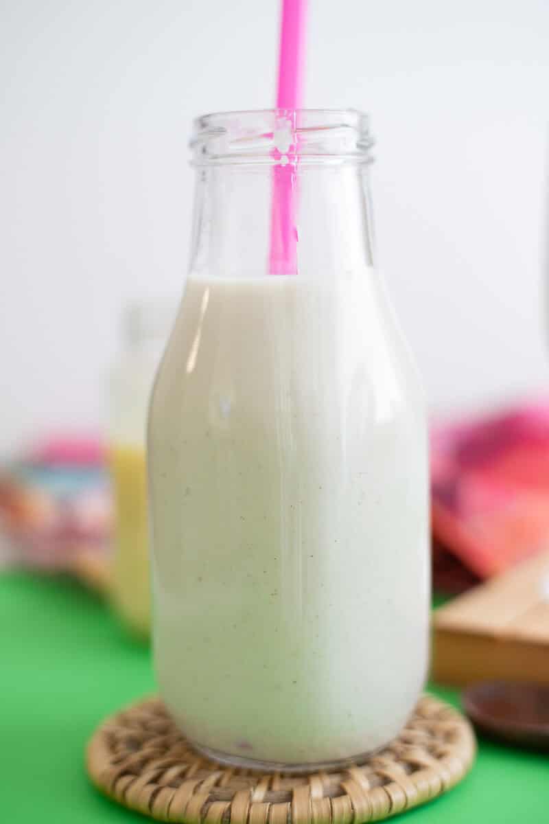 A glass bottle filled with creamy homemade Tobago dasheen punch with a pink straw.