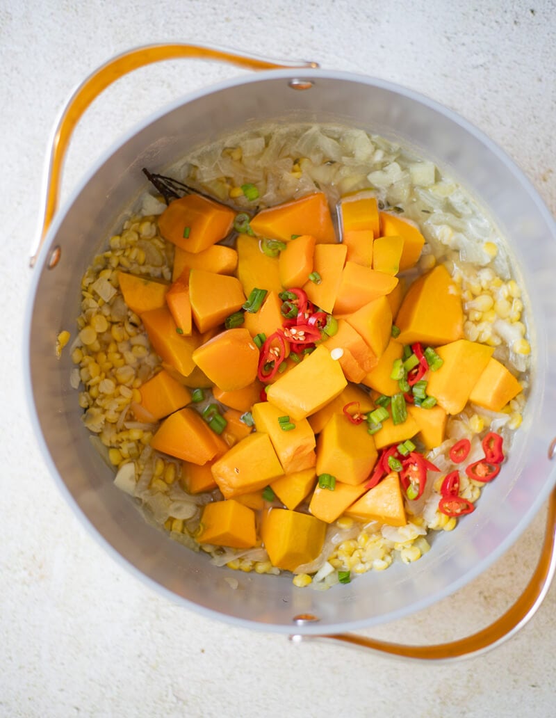 Diced pumpkin, split peas, chopped scallion, and sliced pepper added to a pot for Jamaican pumpkin soup.