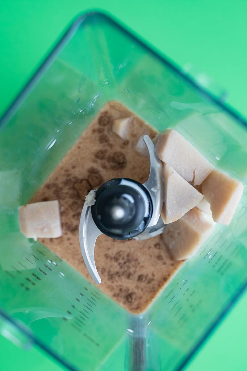 Cubed boiled dasheen, milk, condensed milk, and spices in a blender ready to be mixed.