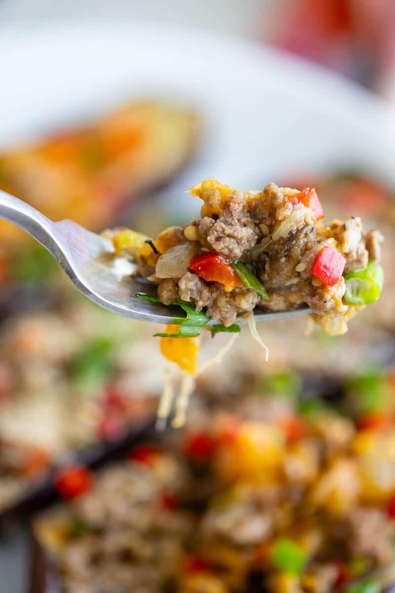 A forkful of filling hovering over a tray of eggplants.