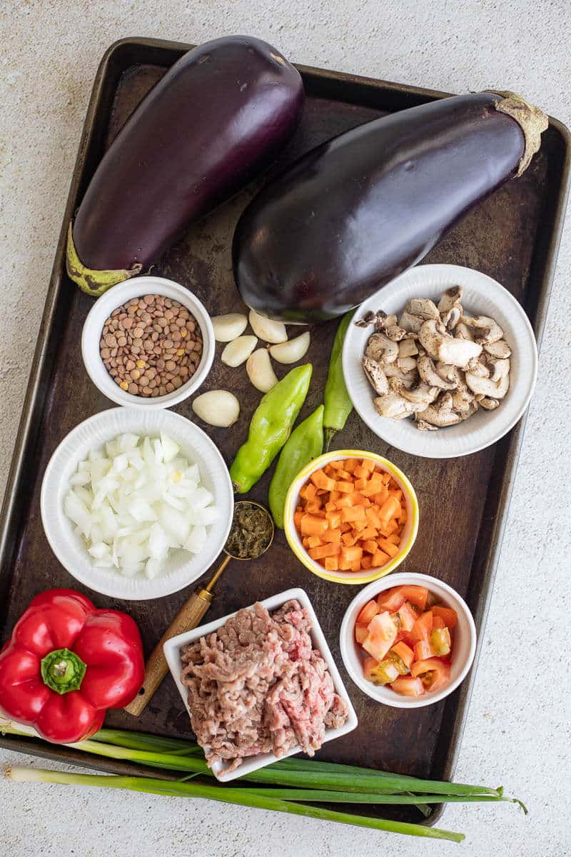 Tray with all ingredients including eggplant, minced meat, mushrooms, lentils, herbs, garlic, peppers, and seasonings