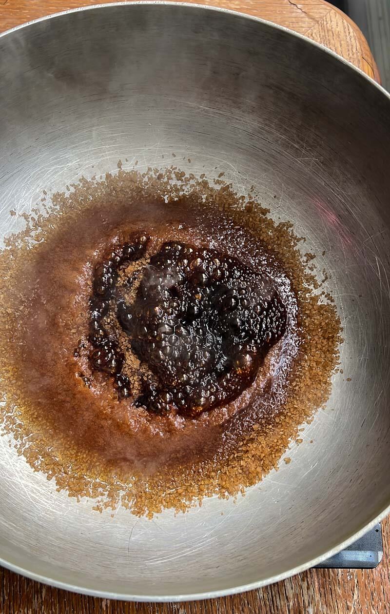Brown sugar bubbling and caramelizing in a pot, showing the correct color for browning sugar Trini style.