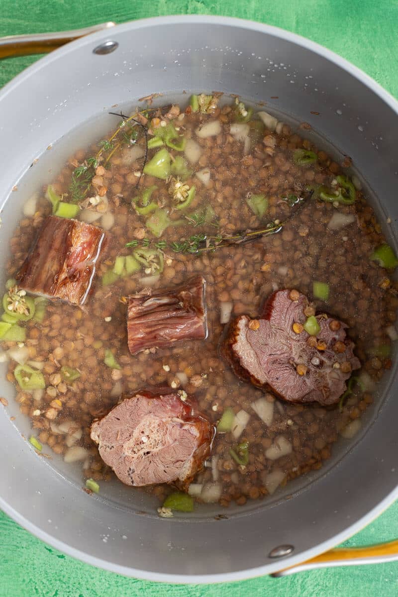 Brown lentils simmering in a pot with thyme, peppers, and salted meat