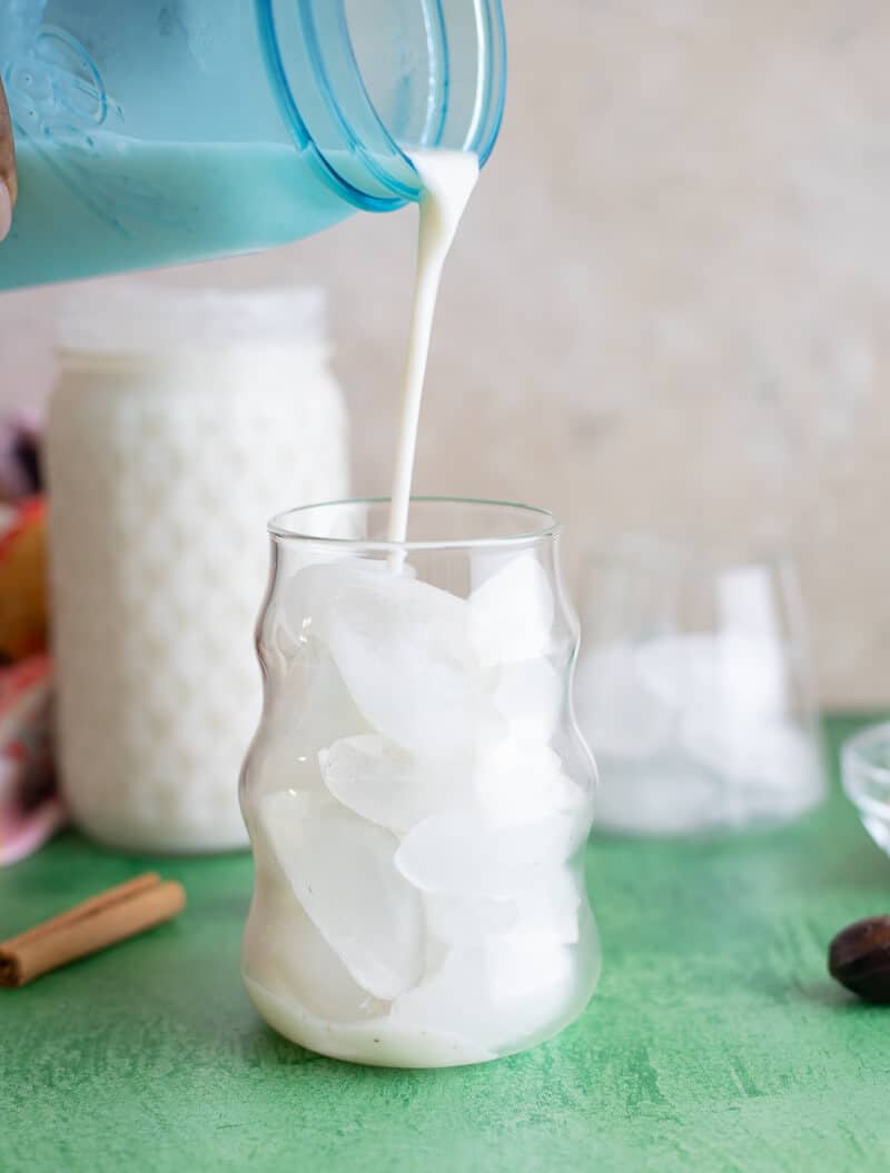 Pouring cassava punch over ice in a glass, showing thick creamy texture.