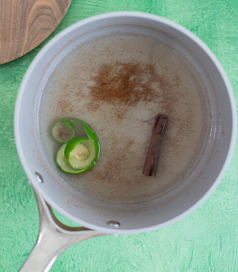 Cinnamon stick, grated nutmeg and lime peel simmering in water to make spiced base.