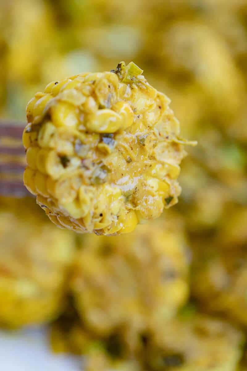 Close-up of a fork holding a piece of Trinidad curry corn coated in curry sauce.