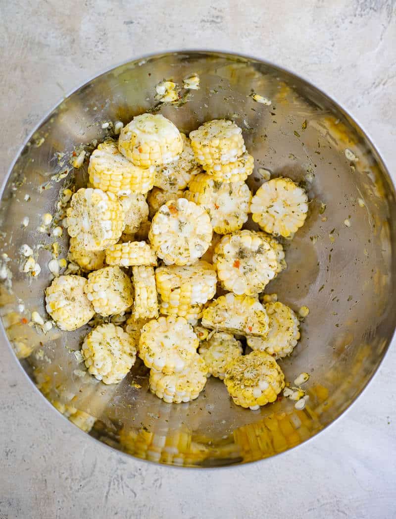 Fresh corn rounds coated with Caribbean green seasoning in a mixing bowl.