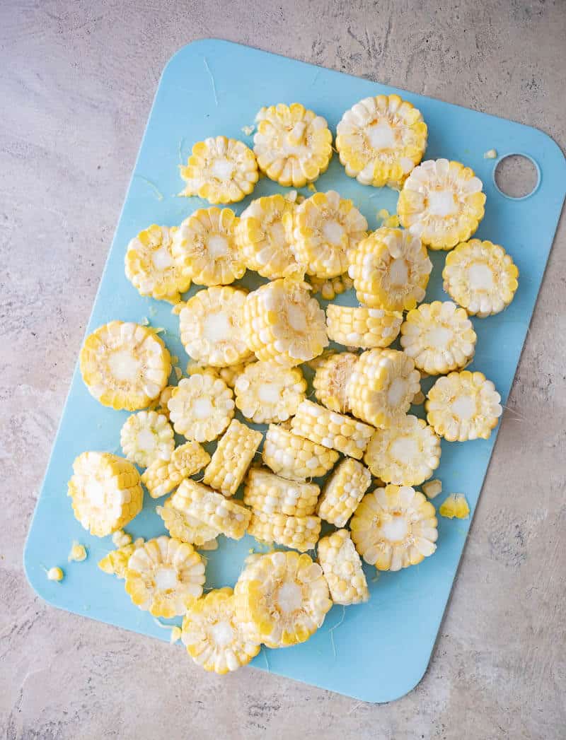 Fresh corn on the cob cut into ¾-inch rounds on a cutting board.