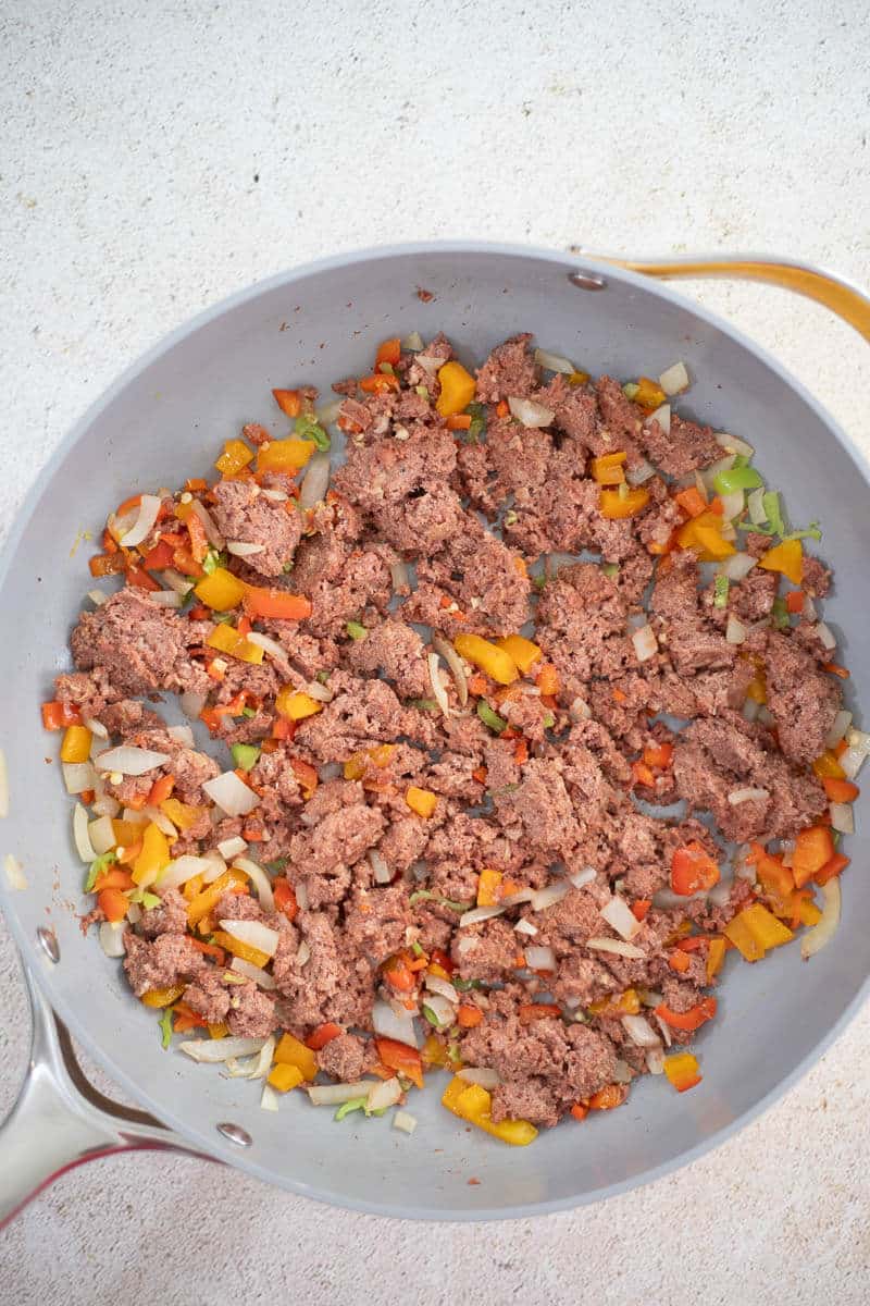 Canned corned beef cooking with onions, bell peppers, and pimento peppers