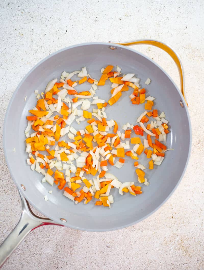 Chopped onions, bell peppers, and pimento peppers sautéing in a pan
