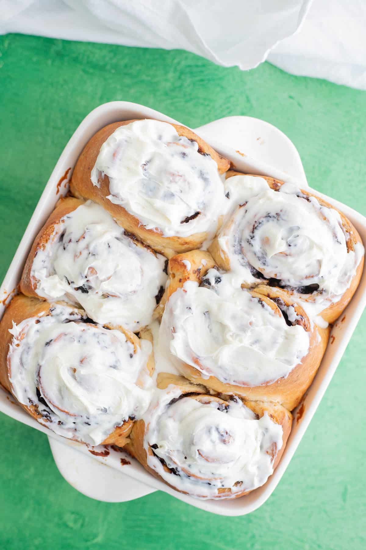 Six baked black cake cinnamon rolls topped with vanilla butter frosting in an 8-inch square pan