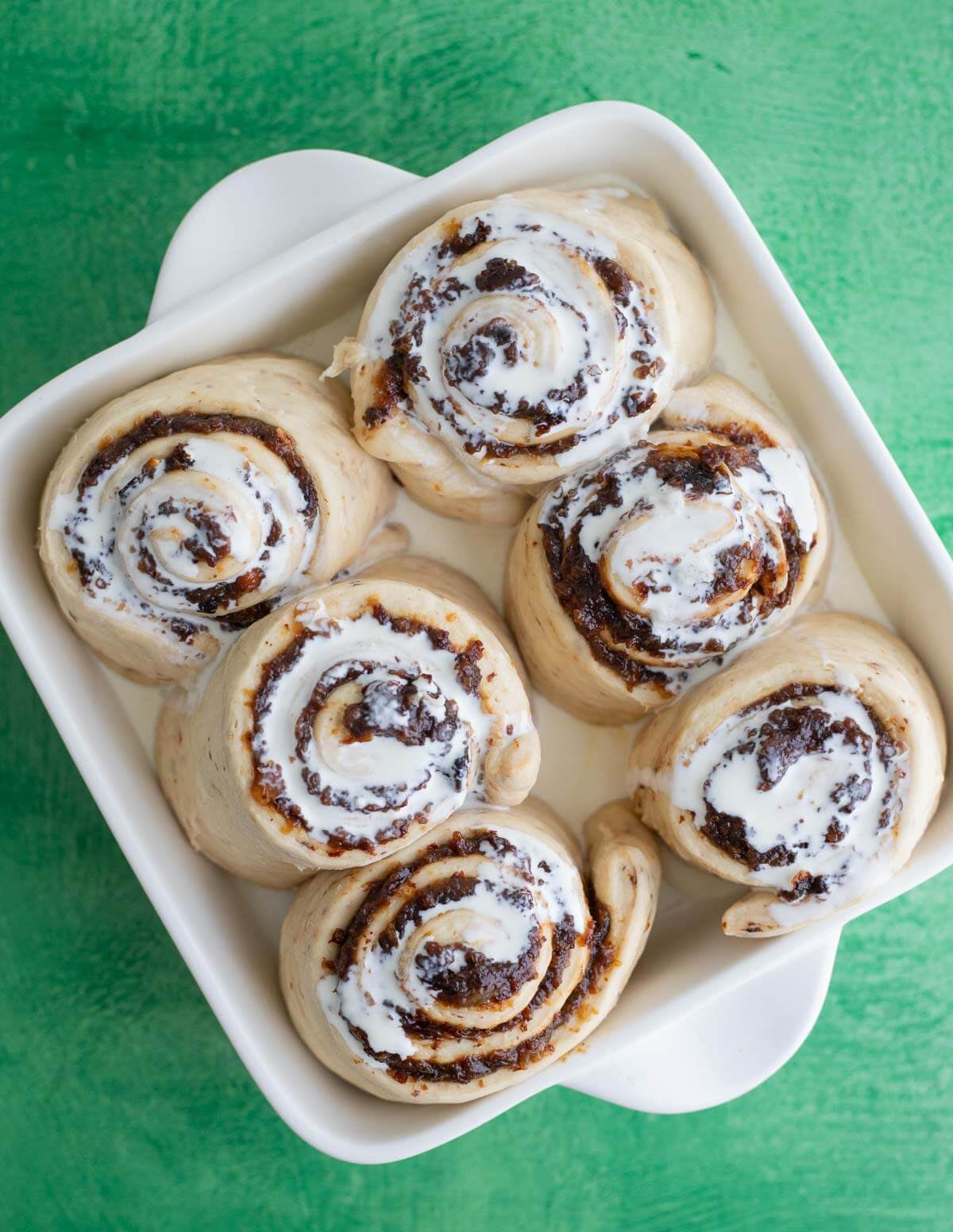 Heavy cream poured over black cake cinnamon rolls before baking
