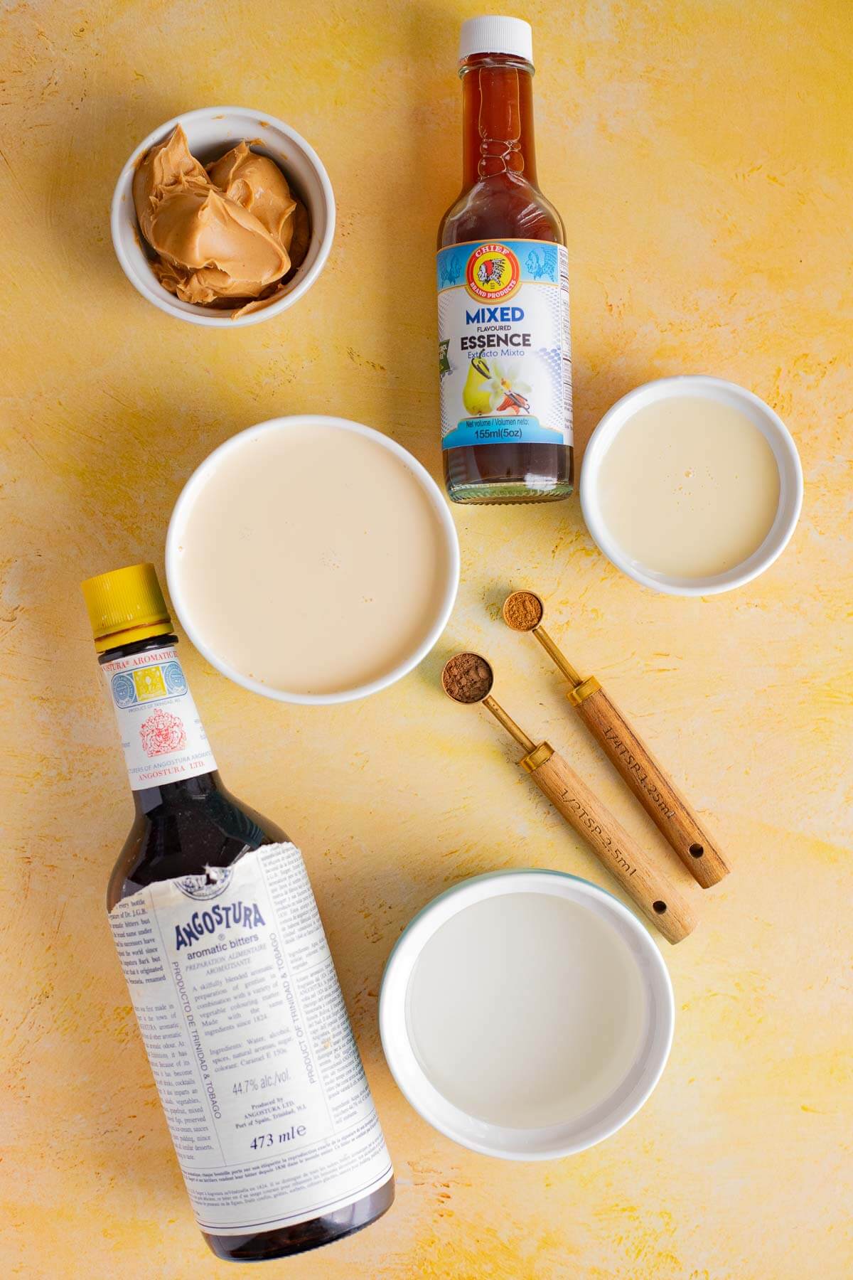 Ingredients for peanut ponche de crème including peanut butter, evaporated milk, condensed milk, spices, bitters, and mixed essence