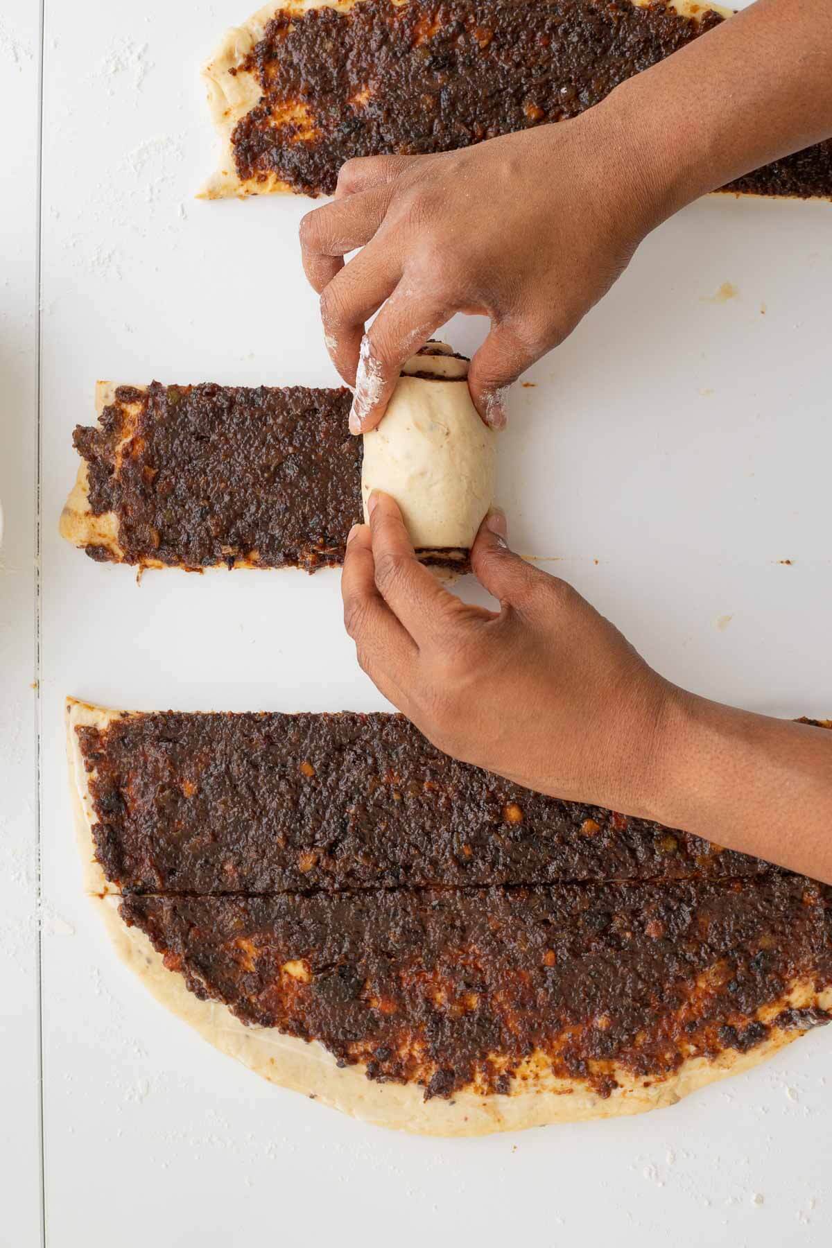 Rolling an individual strip of black cake cinnamon roll dough