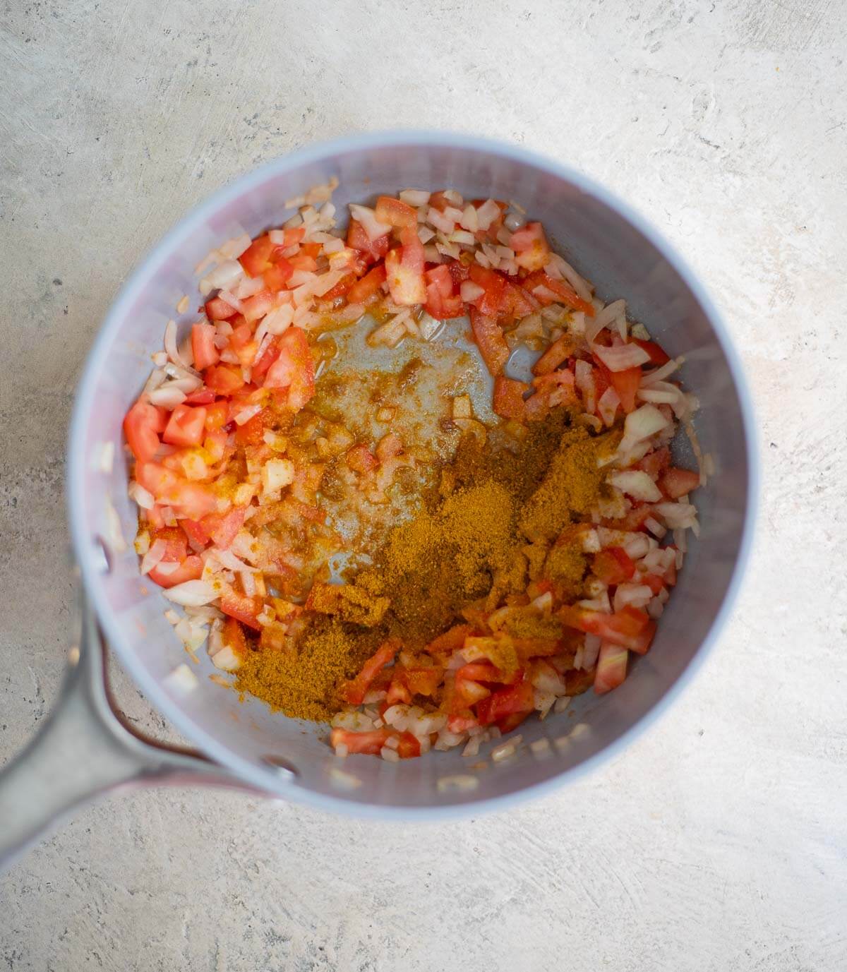 Curry powder added to chopped onion and tomato in a saucepan