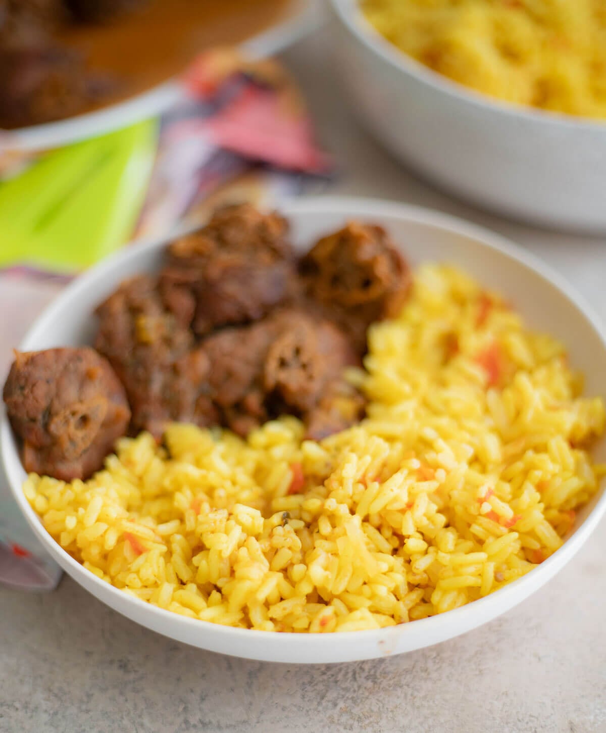 Close-up of fluffy yellow curried rice with small pieces of tomato served alongside stewed turkey neck