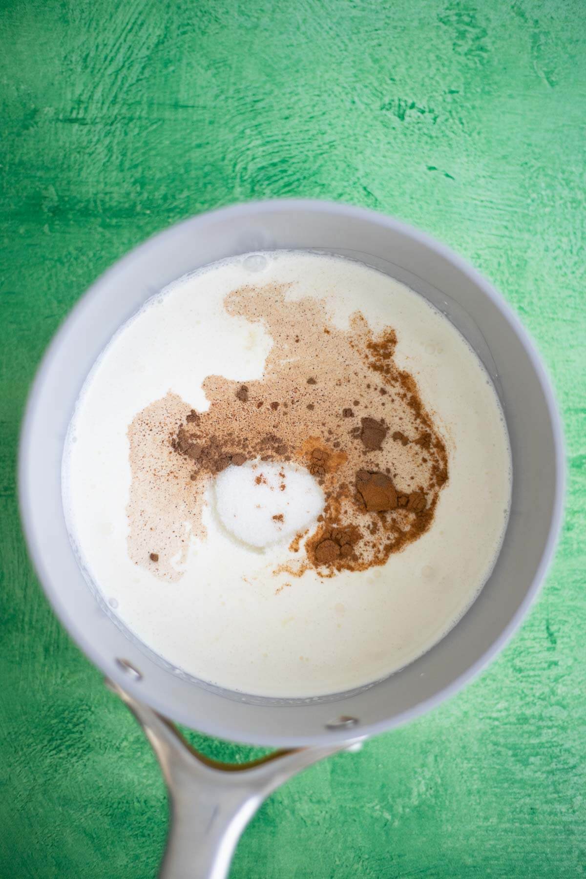 Cinnamon and nutmeg being added to heavy cream in a saucepan to prepare the Ponche de Crème ice cream custard.