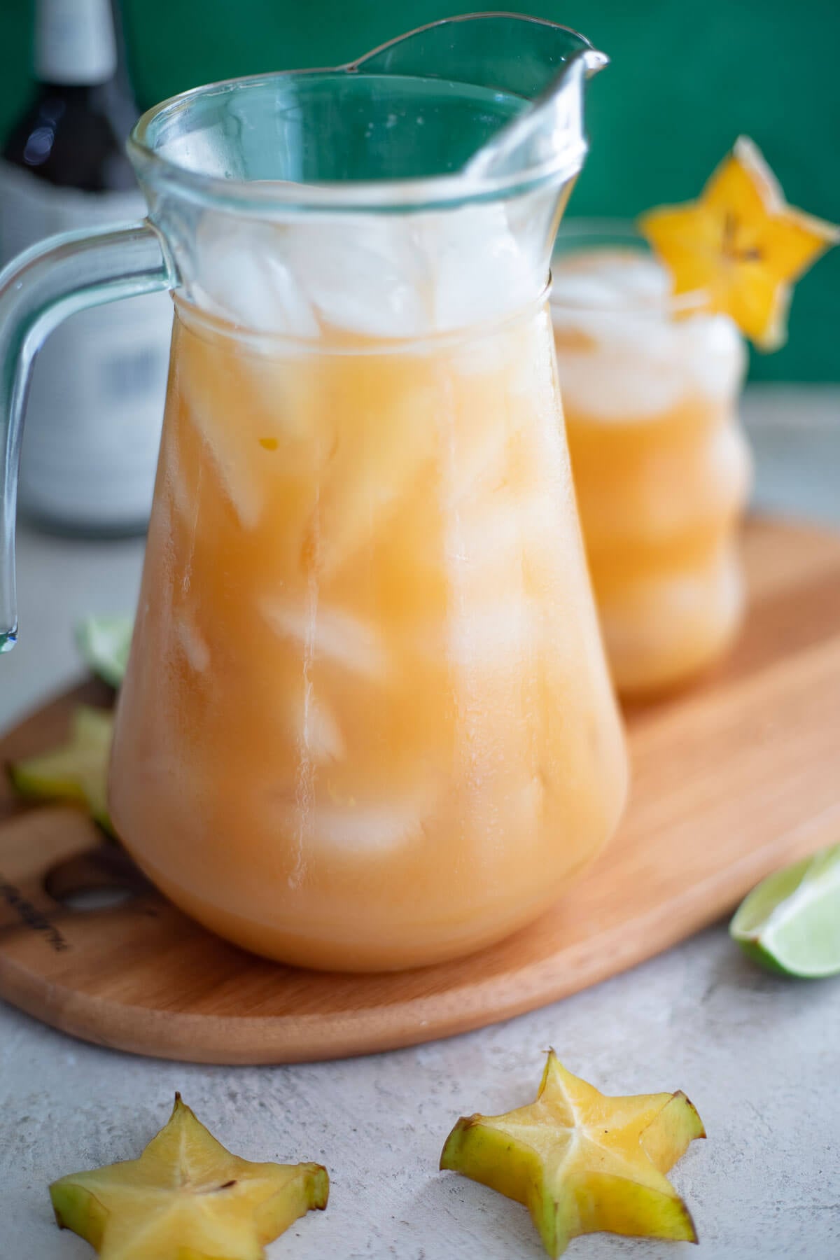 Glass pitcher filled with homemade carambola juice and ice, surrounded by sliced star fruit and lime.