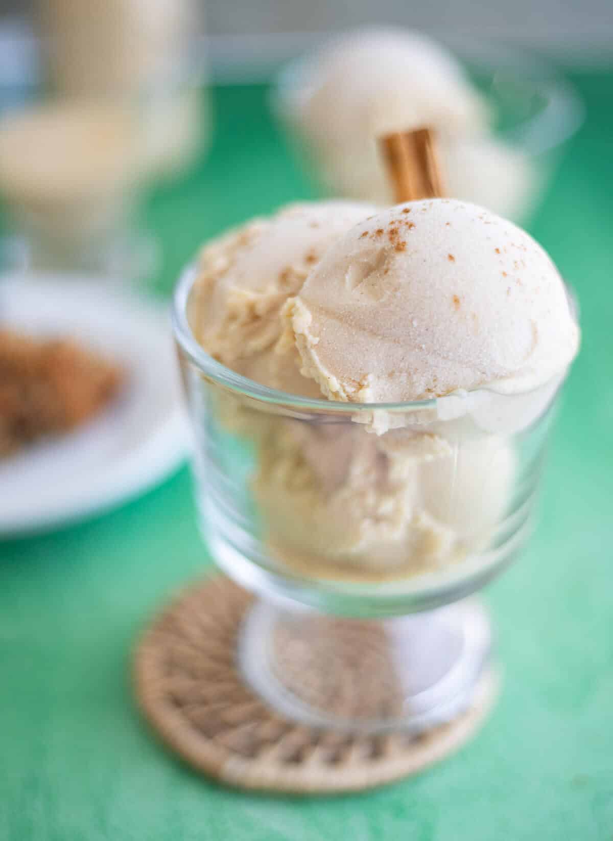 Close-up of homemade Ponche de Crème ice cream scoops topped with a sprinkle of nutmeg in a glass dessert dish.