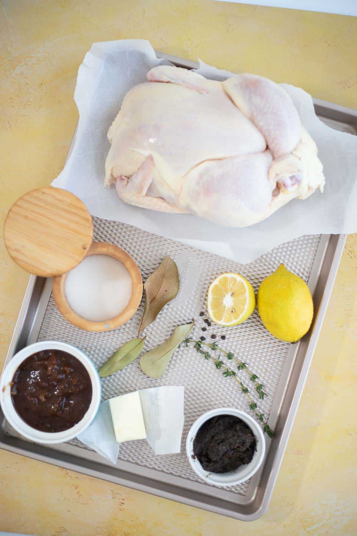 Ingredients for oven baked jerk chicken, including whole chicken, wet jerk seasoning, butter, lemons, herbs, and BBQ sauce.