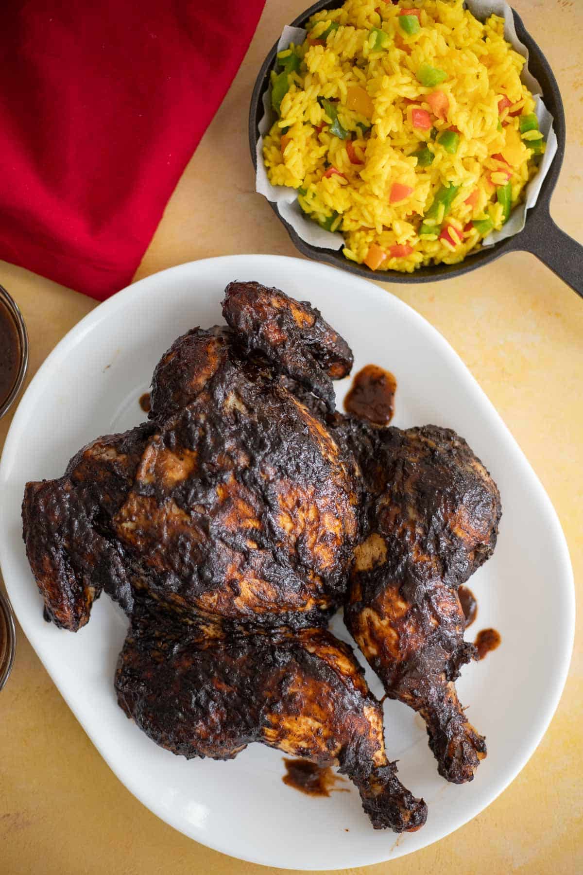 Whole spatchcocked jerk chicken with a dark BBQ glaze served alongside yellow rice.