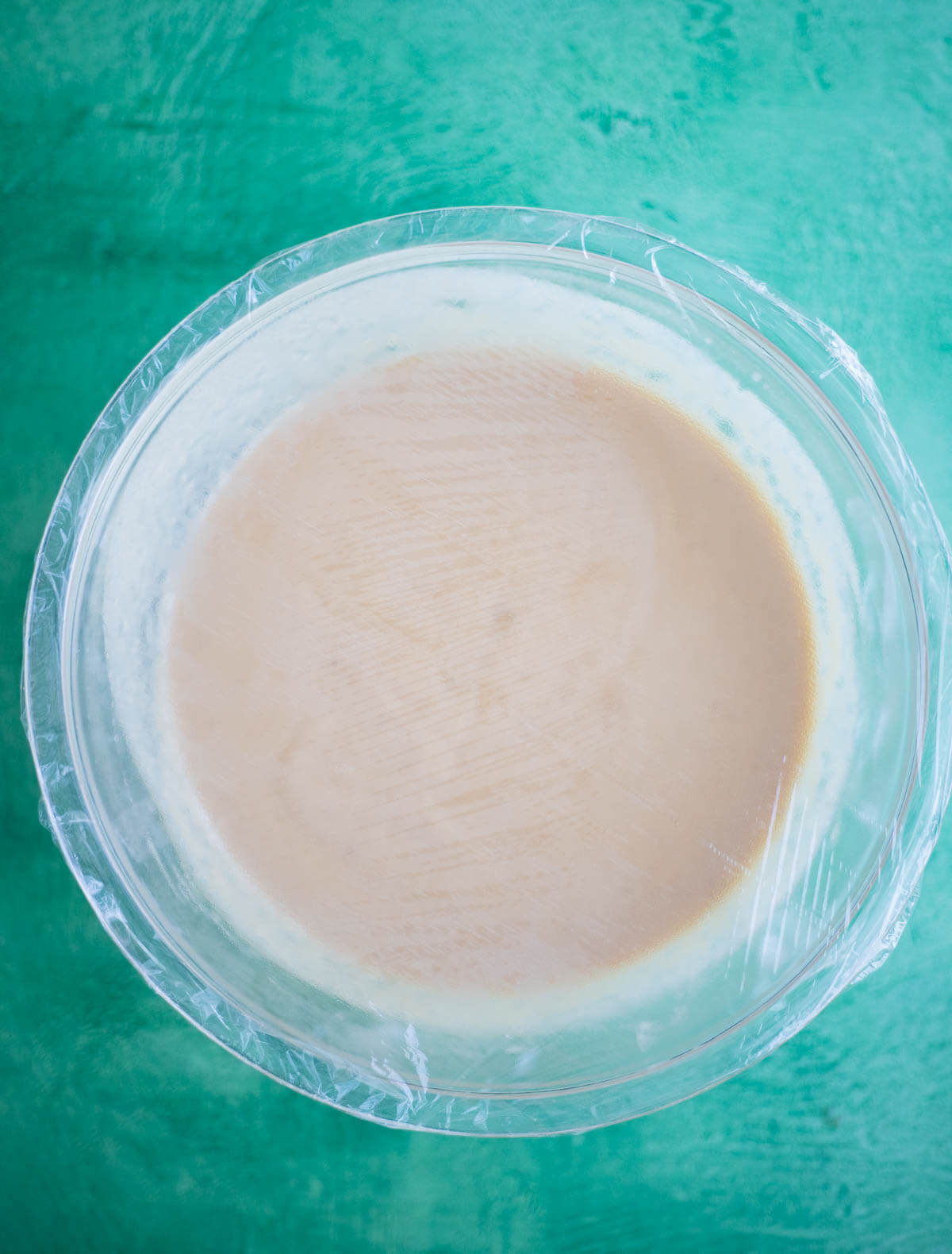Homemade Ponche de Crème ice cream custard covered with plastic wrap in a glass dish before refrigerating.