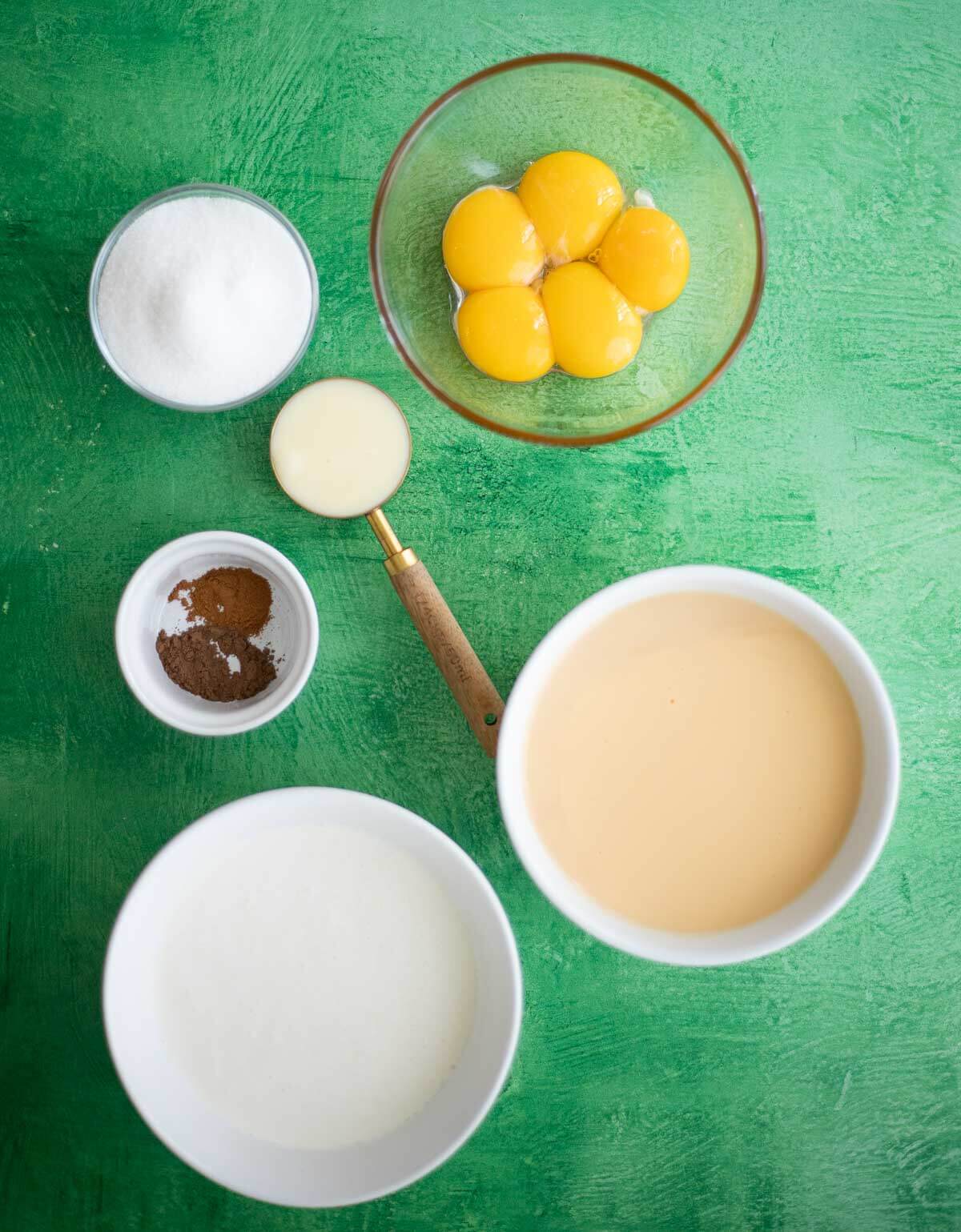 Ingredients for homemade Ponche de Crème ice cream arranged on a countertop, including Ponche de Crème, heavy cream, eggs, condensed milk, sugar, and spices.