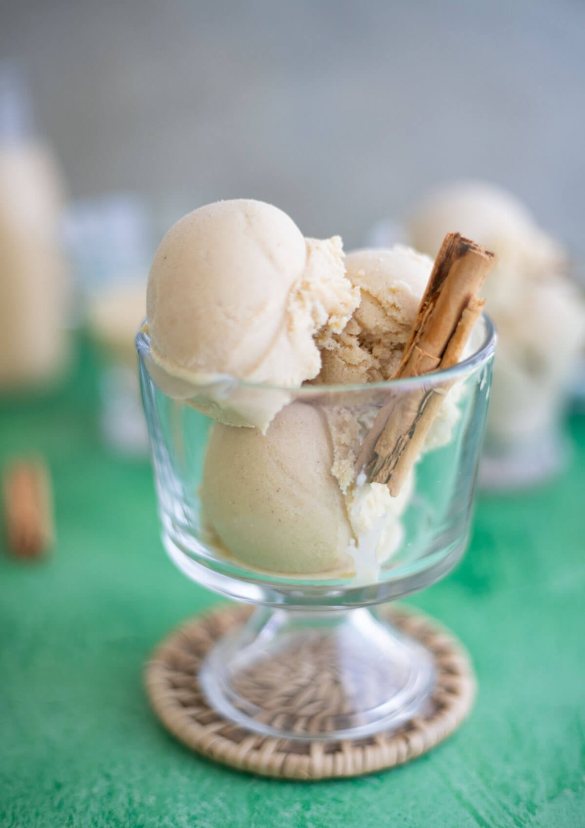 Scoops of homemade Ponche de Crème ice cream in a glass dessert dish with a cinnamon stick.