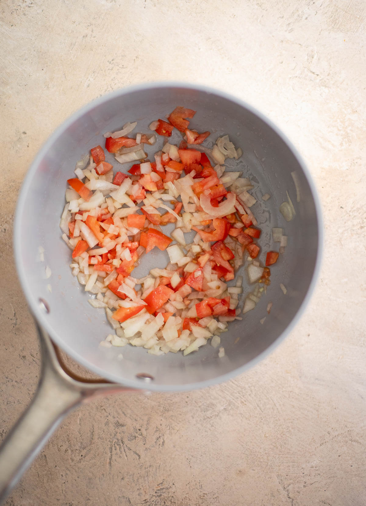 Chopped onion and tomato sautéing in oil in a saucepan