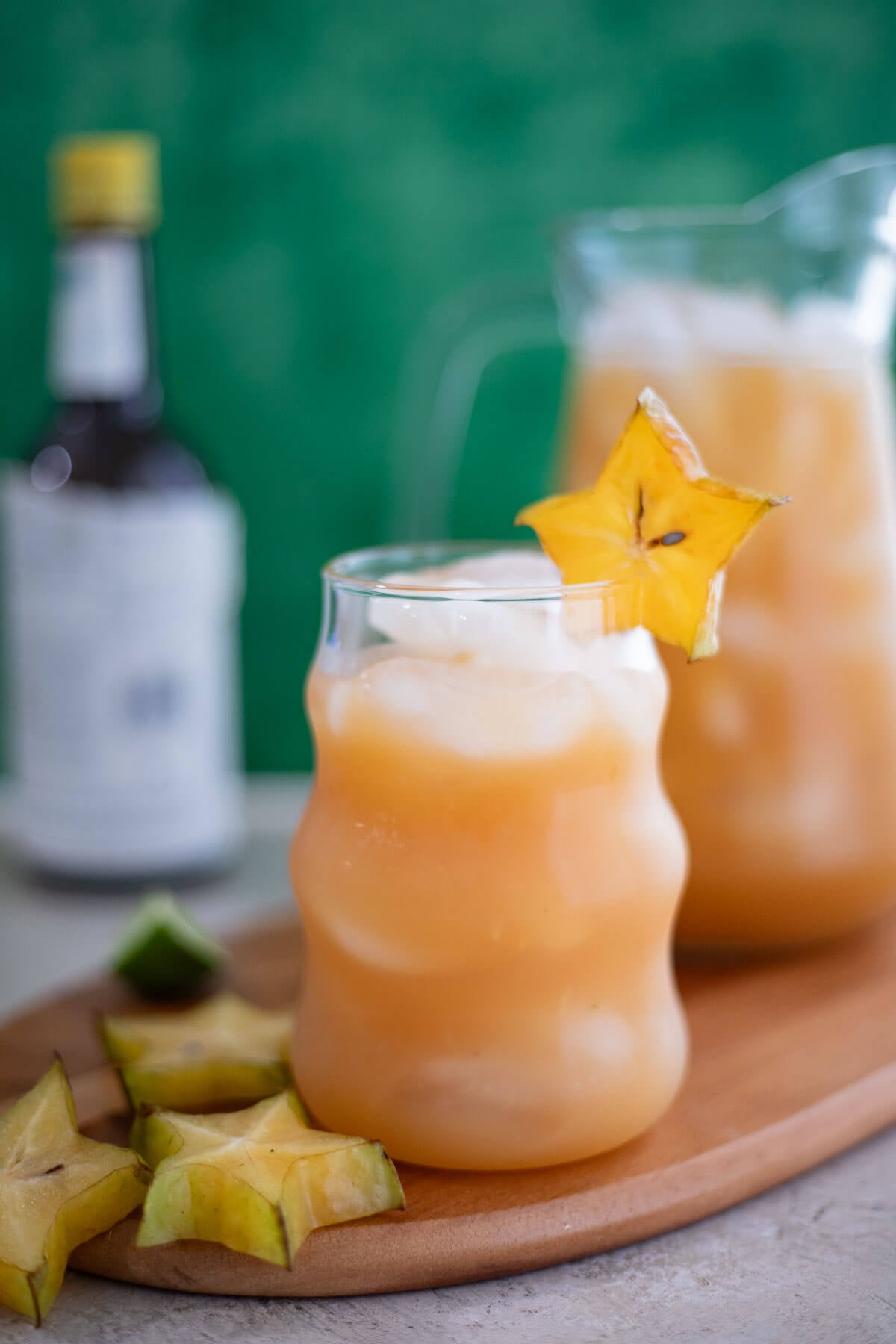 Glass of homemade star fruit juice with ice and a star fruit garnish, with a pitcher in the background.