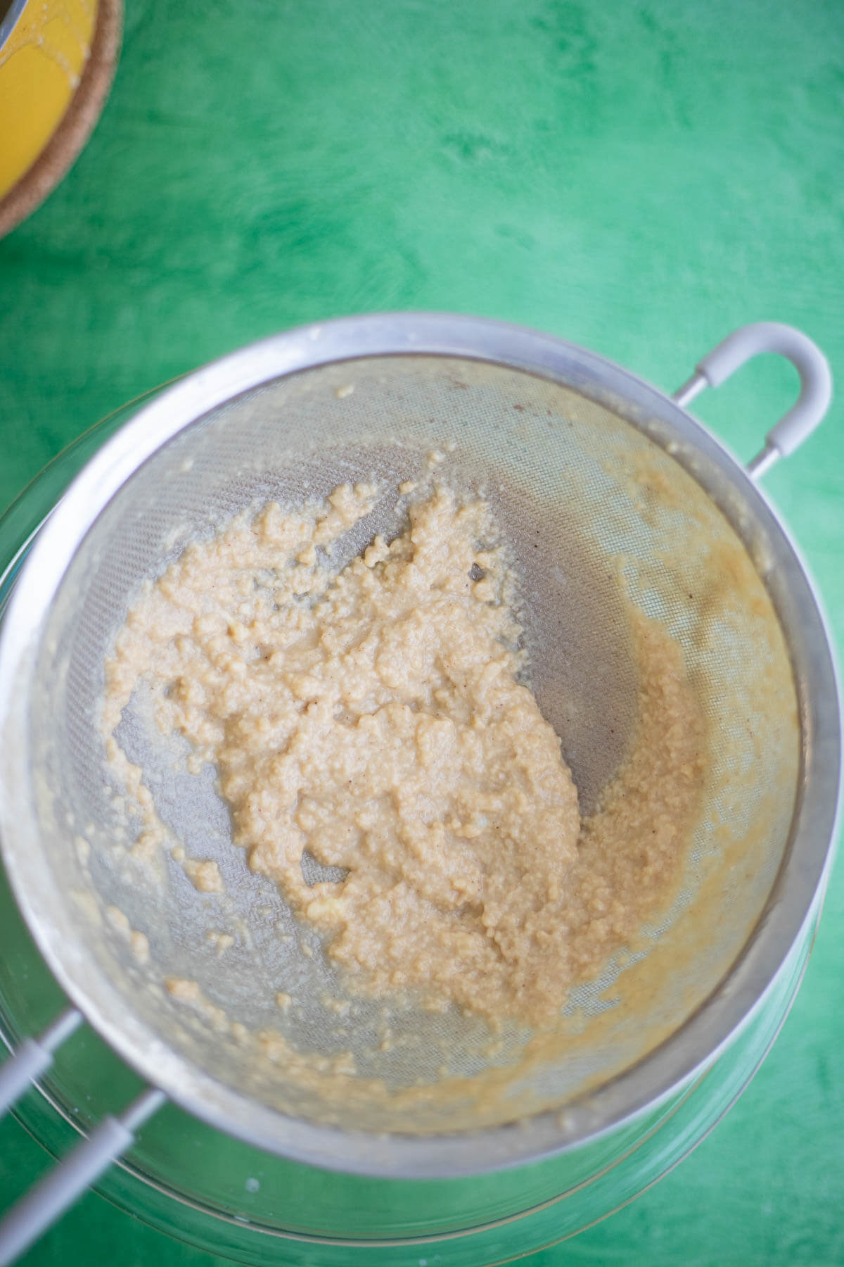 Smooth Ponche de Crème ice cream custard in a glass bowl after being poured through a fine-mesh strainer.