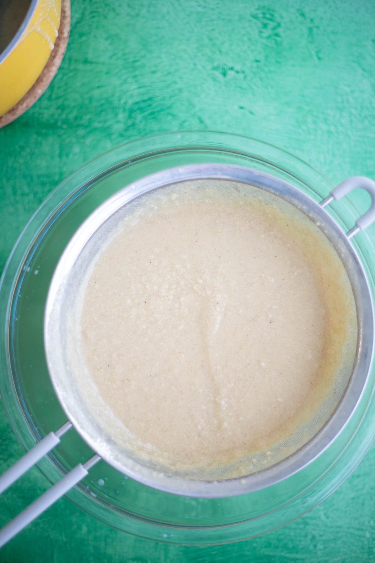 Ponche de Crème ice cream custard being poured through a fine-mesh strainer into a glass bowl.
