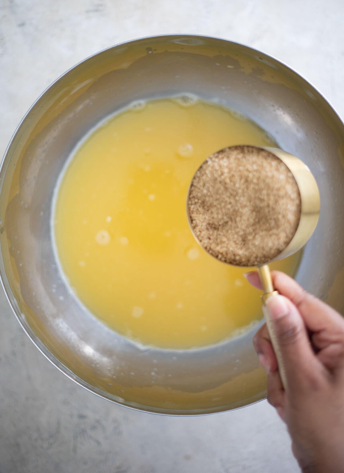Measuring cup of brown sugar held over freshly strained star fruit juice.